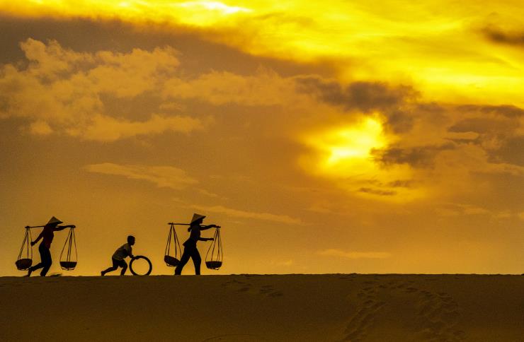 Champa women, walking with a kid creating silhouettes against the sky and soft sand