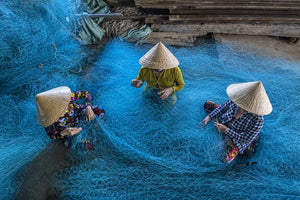 women are weaving and repairing the navy blue fishing nets