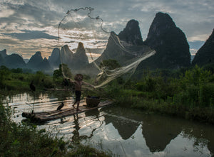 A fisherman throwing a giant fishing net into the water